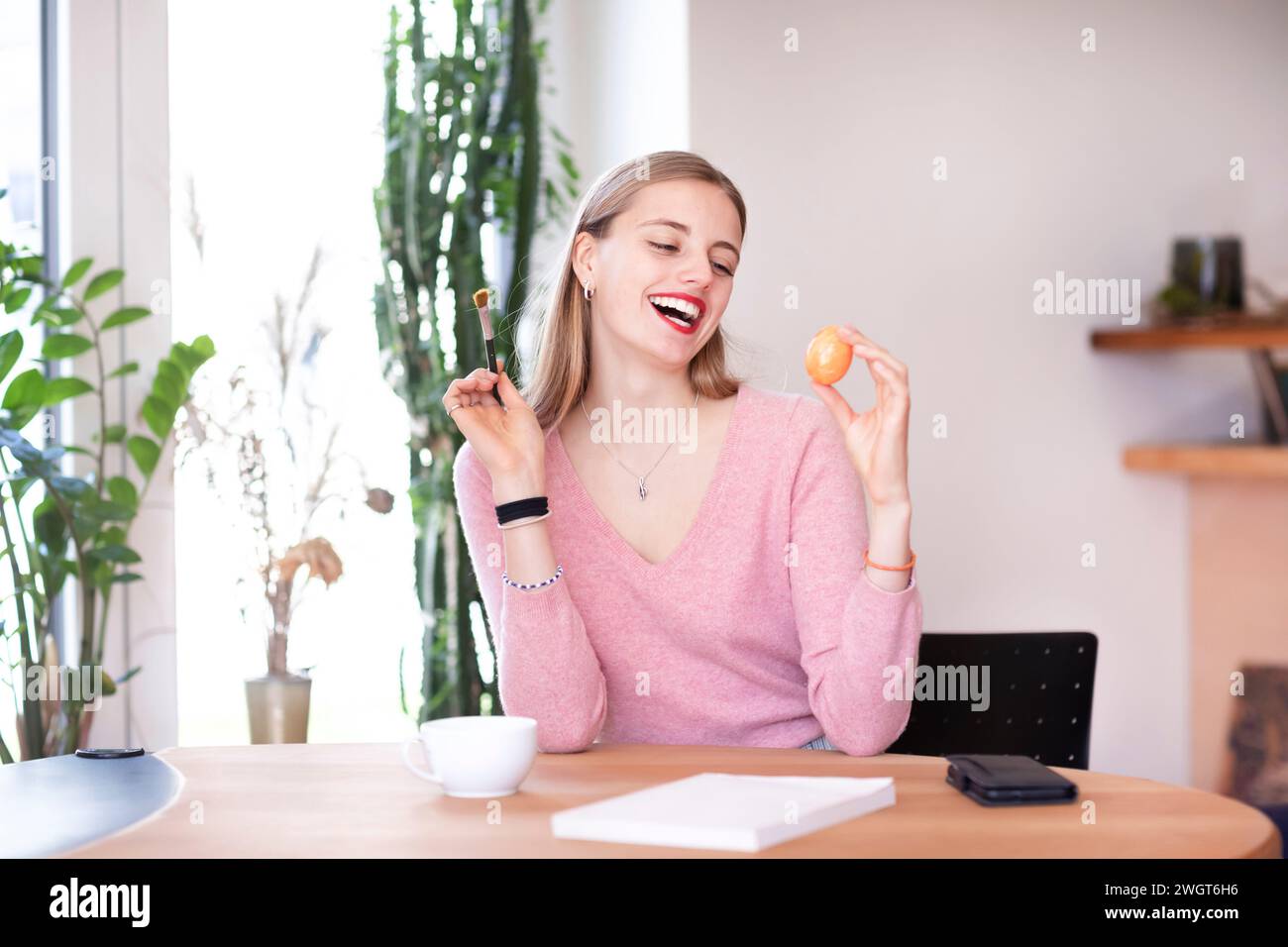 Eine junge Frau mit blondem Haar schminkt sich mit einem Ei Stockfoto