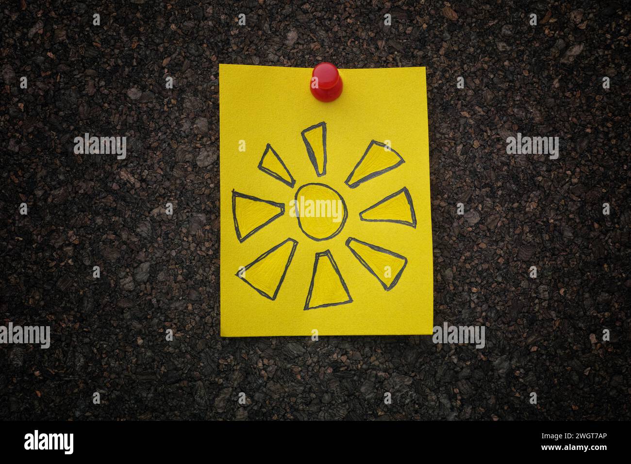 Eine gelbe Notiz aus Papier mit einer Zeichnung der Sonne drauf, die an ein Korkbrett geheftet ist. Nahaufnahme. Stockfoto