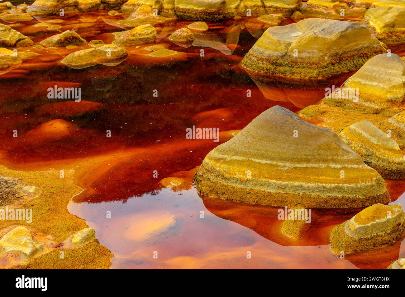 Geschichtete, eisenbeschichtete Steine tauchen aus dem rötlichen, sauren Wasser in der einzigartigen Landschaft von Rio Tinto auf Stockfoto