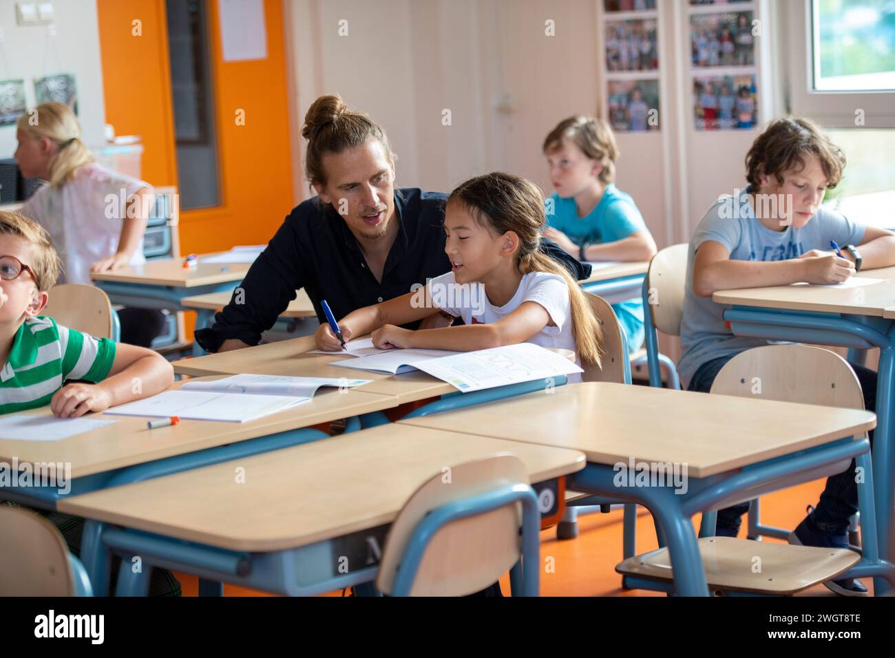 Männlicher Lehrer, der einer Schülerin an ihrem Schreibtisch beim Unterricht hilft Stockfoto