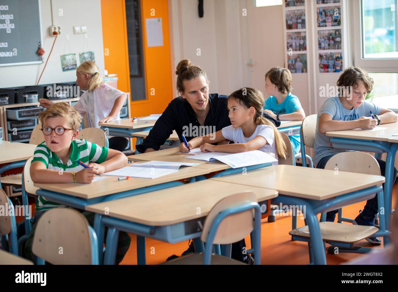 Männlicher Lehrer, der einer Schülerin an ihrem Schreibtisch beim Unterricht hilft Stockfoto