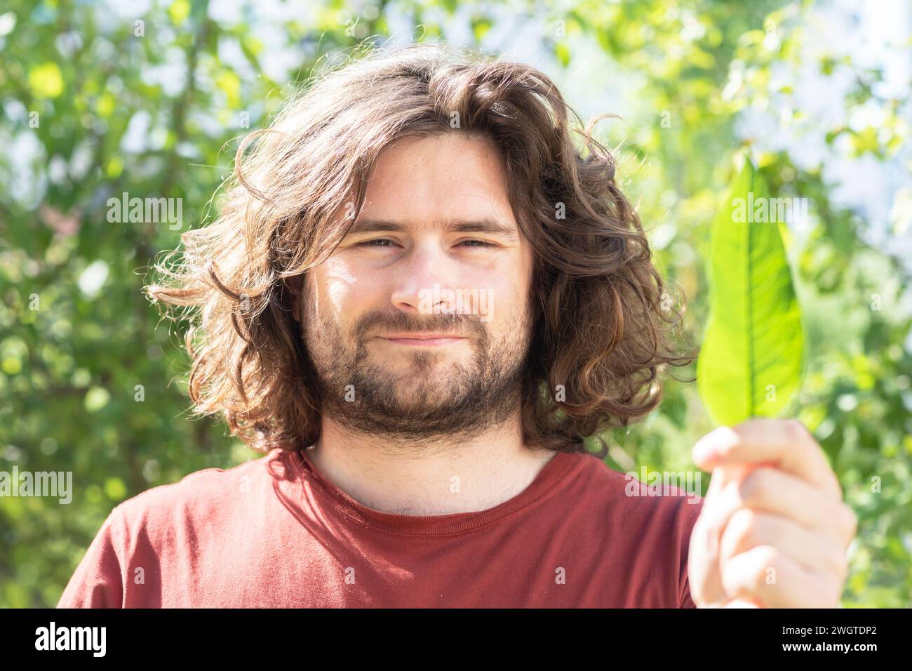 Junger Mann mit einem Blatt in der Hand vor grünen Büschen Klimaschutz Stockfoto