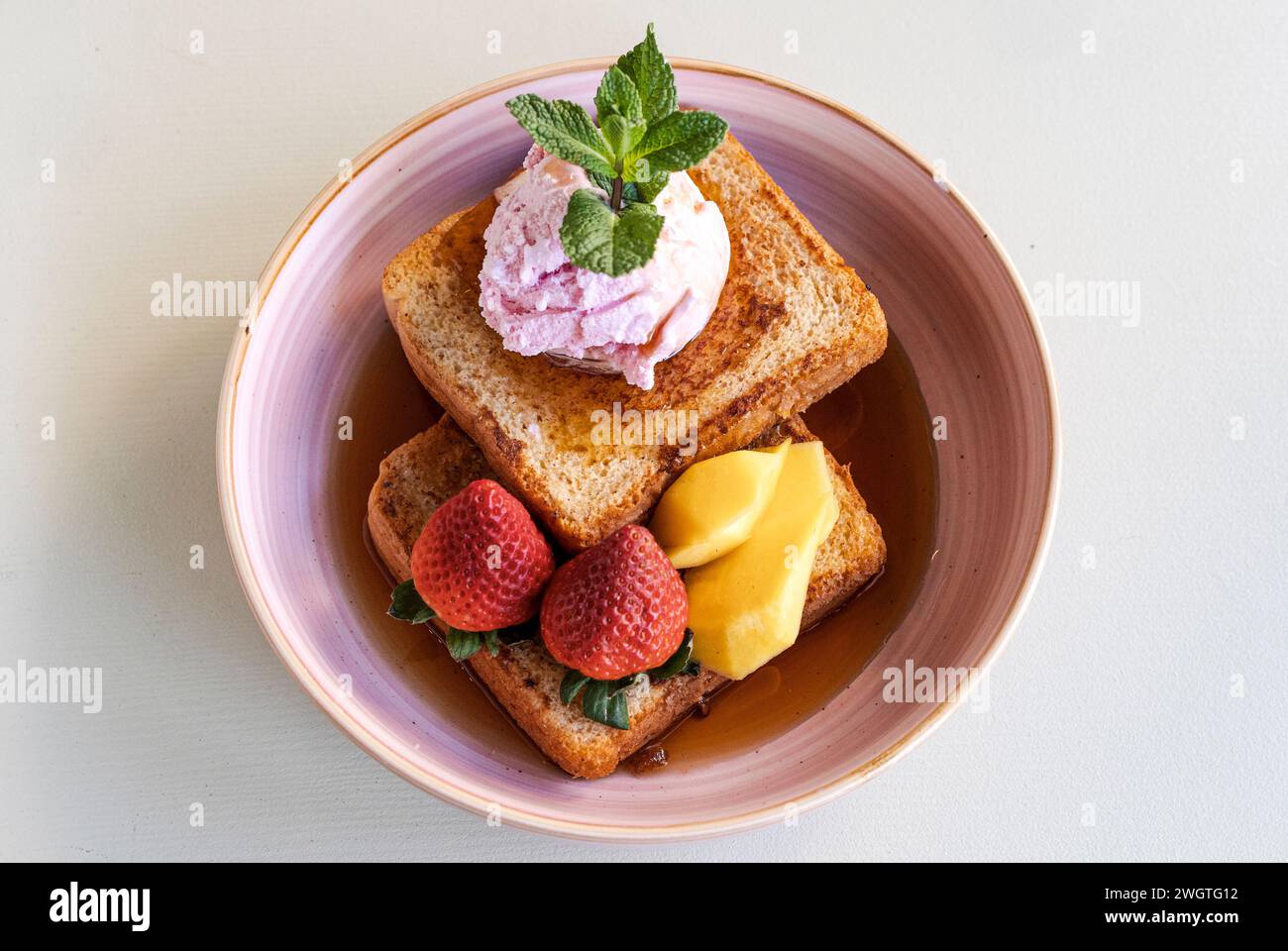 Toast mit Erdbeeren, Mango und Eis mit Ahornsirup in einer Schüssel Stockfoto