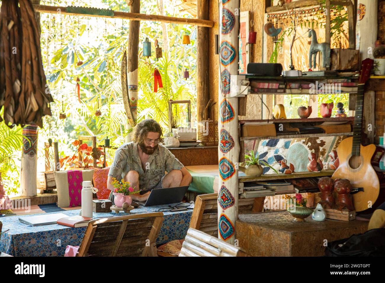 Der junge Mann arbeitet an seinem Laptop und Handy in einem Restaurant in Nordthailand, er ist ein digitaler Nomad, der aus der Ferne arbeitet. Stockfoto