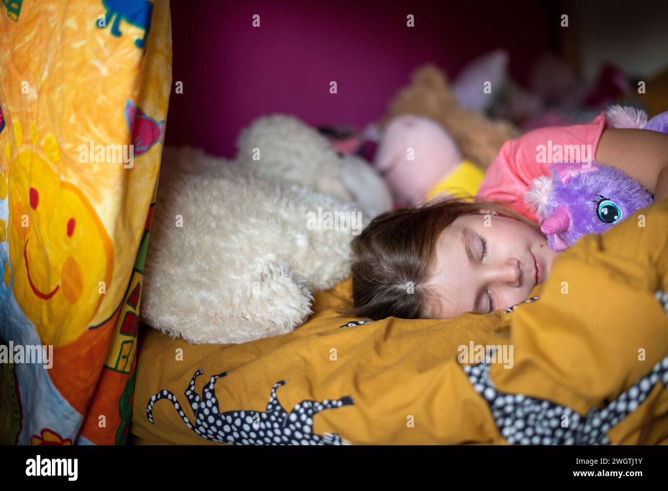 Das junge Mädchen schläft friedlich auf ihrem Bett, umgeben von Teddies Stockfoto