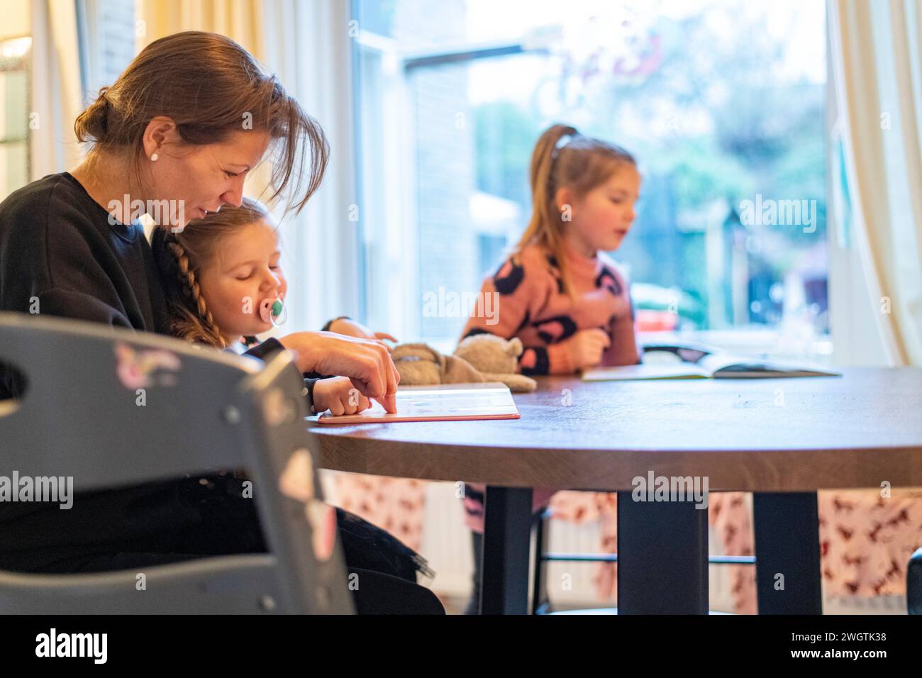 Alleinerziehende Mutter sitzt an ihrem Familientisch mit ihren zwei Mädchen, die ihnen bei ihren Hausaufgaben helfen Stockfoto