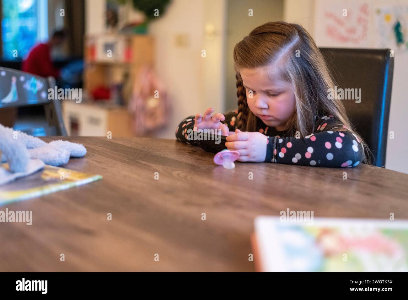 Ein junges Mädchen, das am Tisch des Familienesszimmers sitzt und am Telefon ihrer Mutter spielt. Konzentration beim Versuch, zu gewinnen Stockfoto