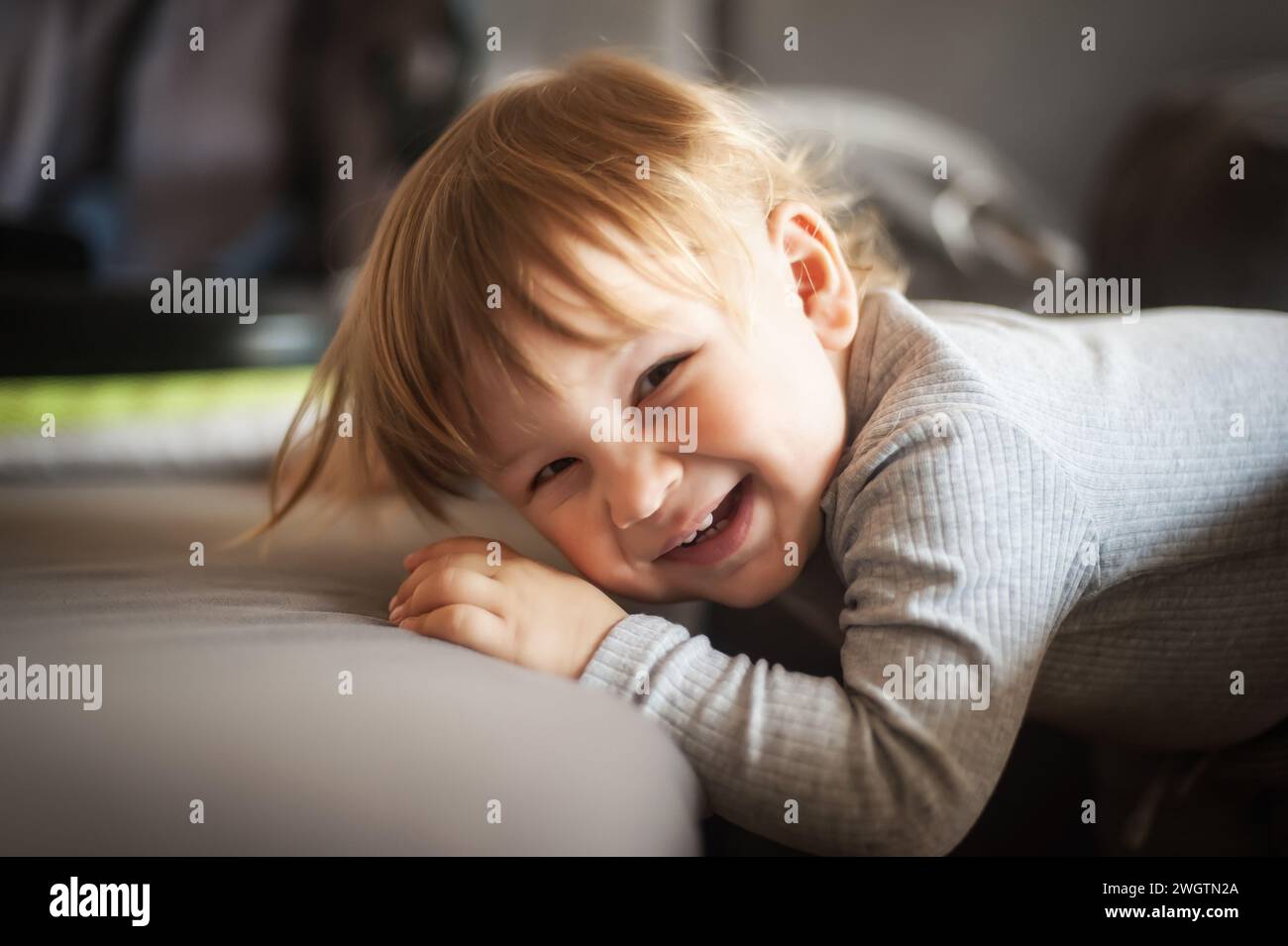 Porträt eines glücklichen, süßen, lächelnden Jungen, der sich auf der Couch beugt und in die Kamera schaut. Freude und Glück Konzept. Liebe und familiäre Emotionen Stockfoto