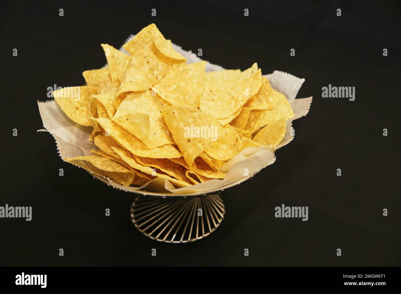 Knusprige goldene Tortilla Chips in dekorativer Schüssel vor schwarzem Hintergrund Stockfoto