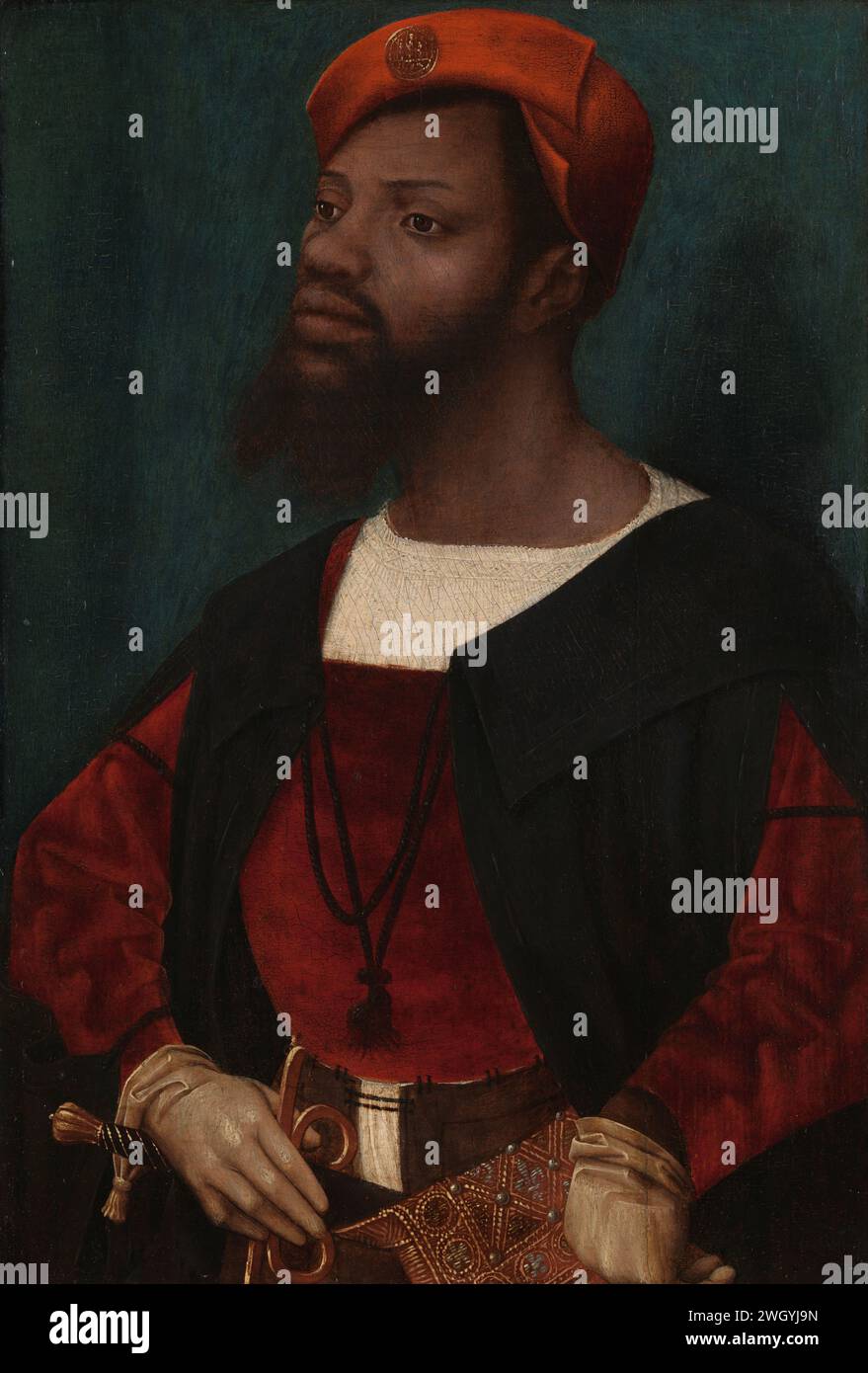 Porträt eines Afrikaners, ca. 1525 - ca. 1530 Gemälde eines Afrikaners in europäischer Kleidung. Stehend, halbiert, drei Viertel links, mit blaugrünem Hintergrund. Er trägt eine rote Baskenmütze (Klappap), auf der ein Pilgersinzeichen aus Onze-Lieve-Vrouwe van Halle bei Brüssel steht. Der Mann hat einen Schnurrbart und einen Bart, der in zwei Punkten endet. Er trägt ein weißes Hemd ohne Kragen, über dem ein roter Wambuis und ein kurzer schwarzer Mantel (Taboling) und weiße Ziegenlederhandschuhe liegen. Mit seiner rechten Hand umfasst er das Reich, das von seinem Schwert bearbeitet wurde. Seine linke Hand auf seiner Seite. Eine reich gestickte Tasche auf seinem L Stockfoto