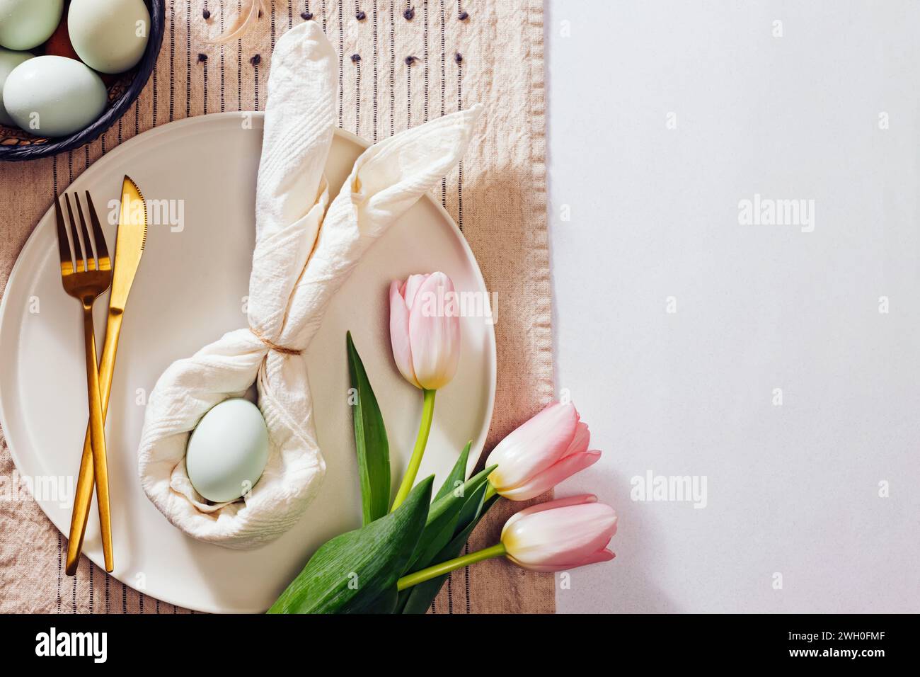 Ostertisch, Serviette in Form eines Kaninchens gefaltet, blaues Ei und rosa Tulpen. Stillleben im Frühling, Draufsicht Stockfoto