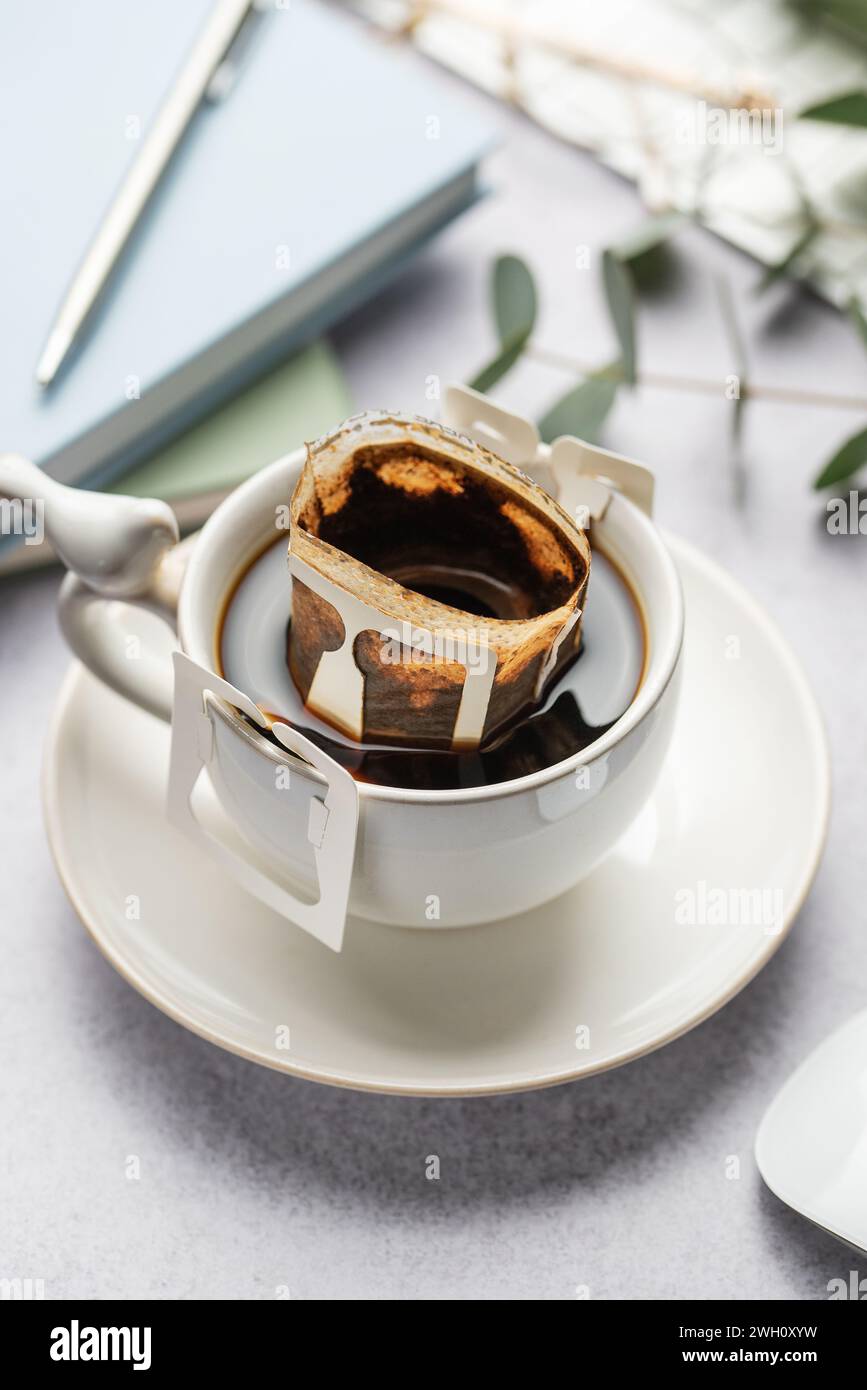 Eine Glasschale frisch gebrühten Kaffees mit einem praktischen Tropfkaffefilter auf dem Bürotisch. Kaffeepause, schnelle Art, heißes Getränk zuzubereiten Stockfoto