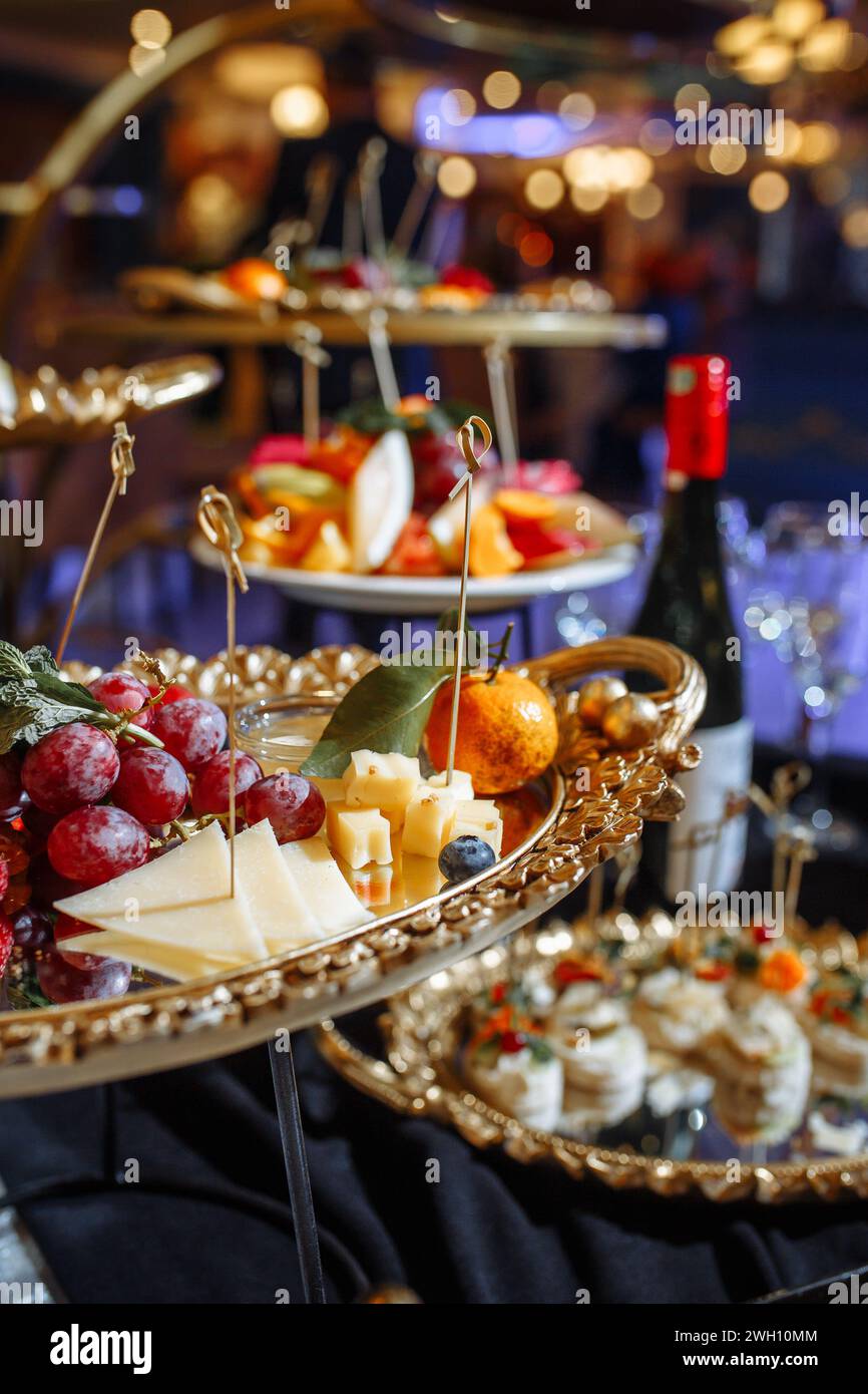 Eine Auswahl an frischem Obst und Käse ist elegant auf goldenen Platten angeordnet, um eine optisch ansprechende und köstliche Präsentation zu schaffen. Perfekt für Stockfoto