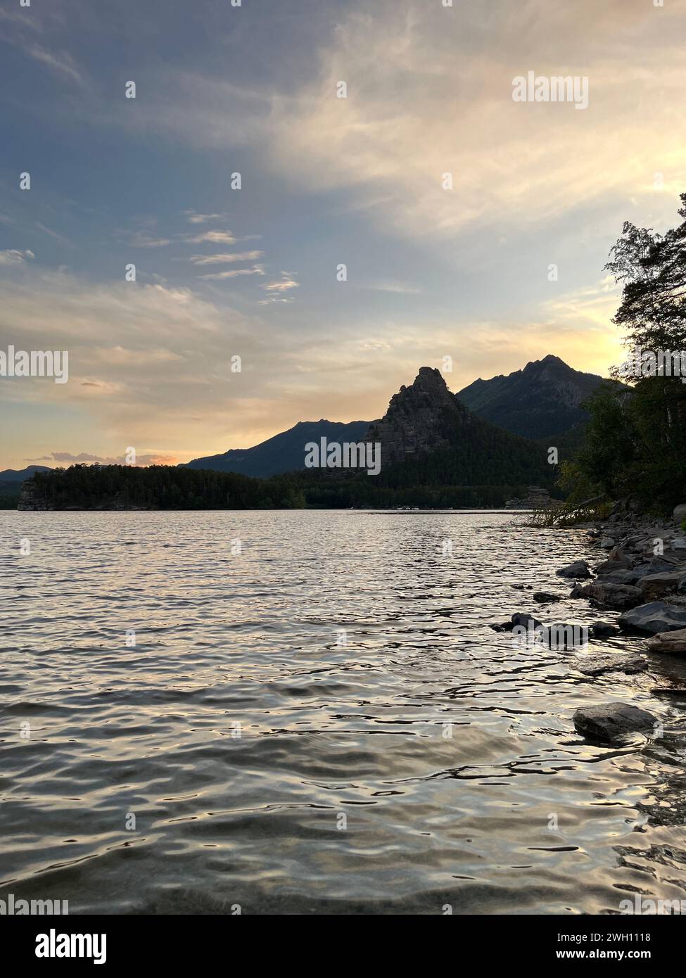 Ein ruhiger Abend mit Bergen, einem ruhigen See und üppigen Bäumen. Sanfte Farben reflektieren das Wasser und schaffen eine faszinierende natürliche Schönheit. Entspannen Sie sich und genießen Sie n Stockfoto