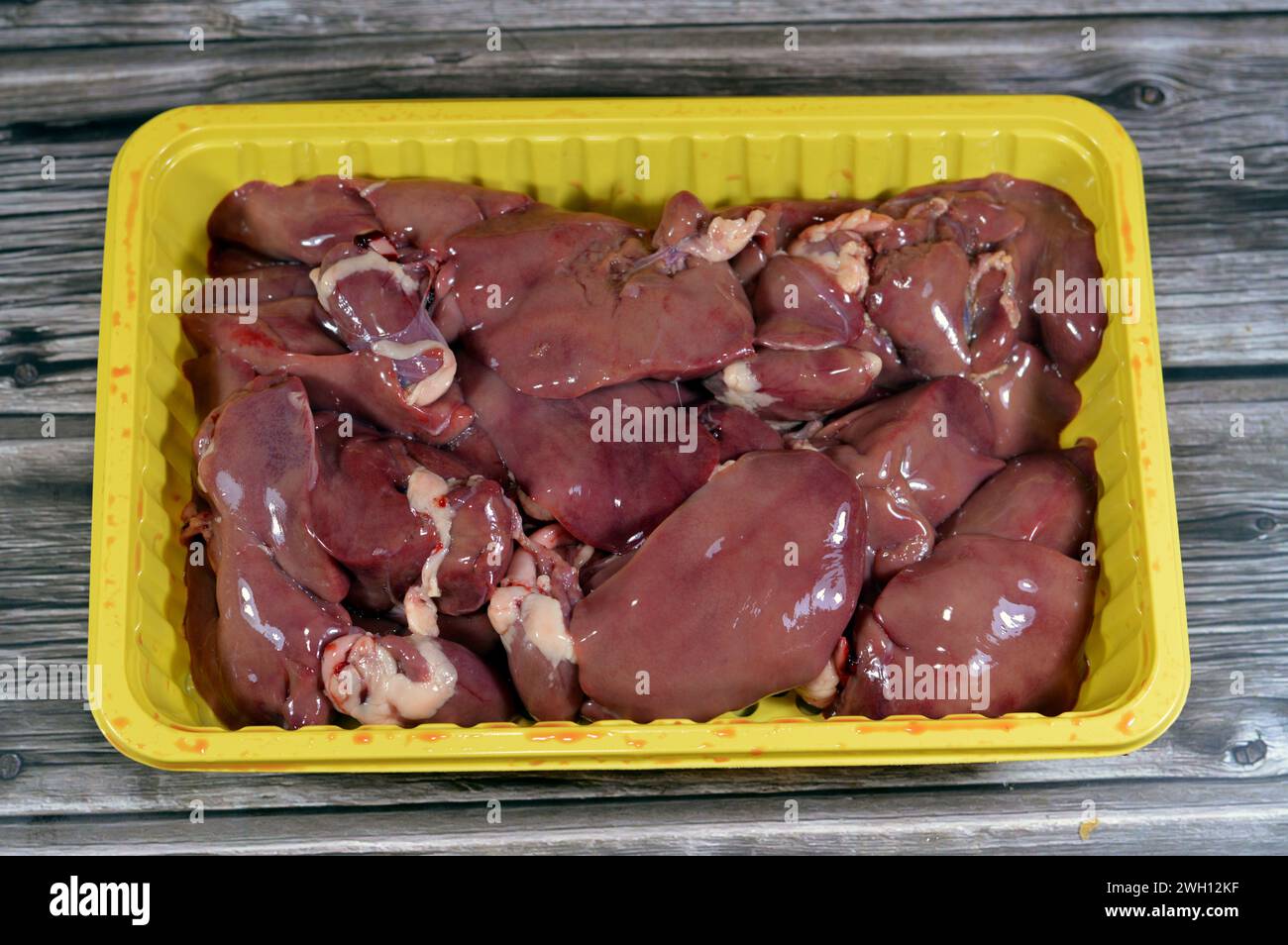 Rohe Hühnerlebern, Magen und Herzen, frische Leber, Magen und Herz von Hühnern voller Eiweiß auf einer gelben Einwegplatte isoliert auf Holzbaa Stockfoto