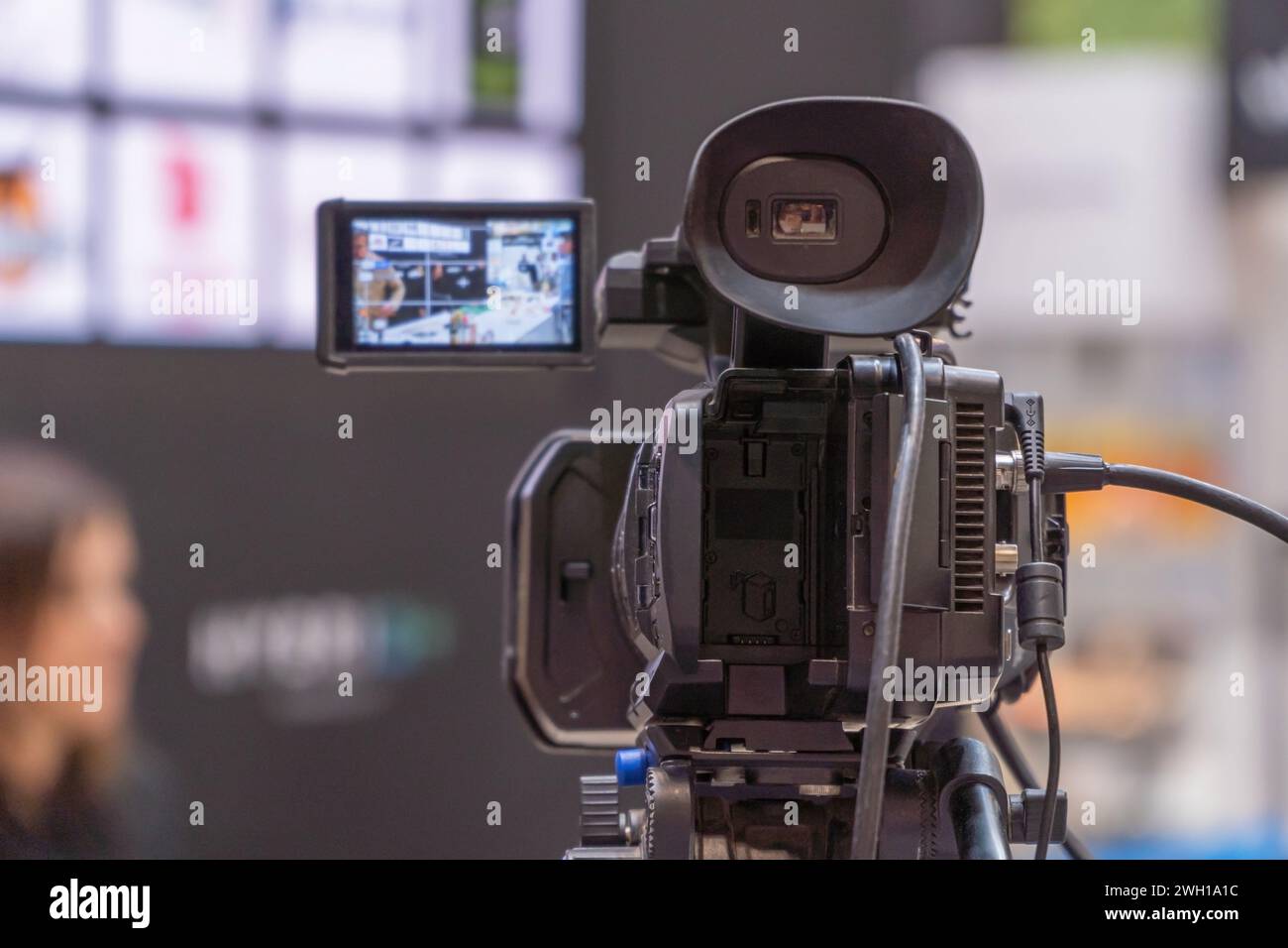 Eine High-Definition-Fernsehkamera mit Überwachungsbildschirm erfasst einen Live-Stream in einem geschäftigen Messezentrum und fokussiert auf einen Unidentif Stockfoto