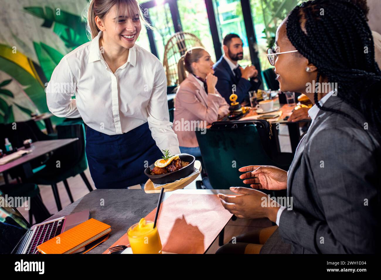 Lächelnde Kellnerin serviert im Restaurant eine Mahlzeit für Geschäftsfrau. Stockfoto