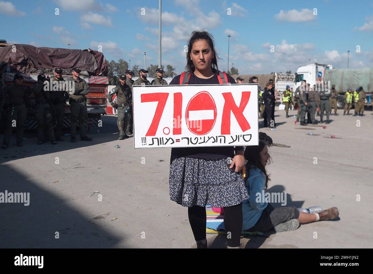 Ein Demonstrant hält ein Schild mit der Aufschrift „humanitäre Hilfe = Tod“, während rechte israelische Demonstranten ägyptische Lastwagen blockieren, die humanitäre Hilfsgüter in den Gazastreifen auf der israelischen Seite des Grenzübergangs Karem Abu Salem transportieren, auch bekannt als der Grenzübergang Kerem Shalom am 6. Februar 2024 in Kerem Shalom, Israel. Seit einigen Tagen blockieren israelische Siedler LKW, die humanitäre Hilfsgüter für Palästinenser im belagerten Gazastreifen transportieren. Stockfoto