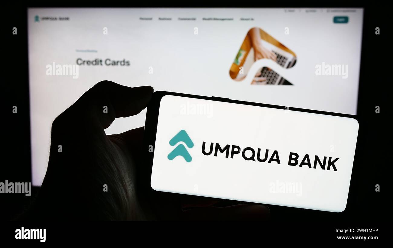 Person mit Smartphone und Logo des US-Finanzdienstleisters Umpqua Bank vor der Website. Schwerpunkt auf dem Display des Telefons. Stockfoto