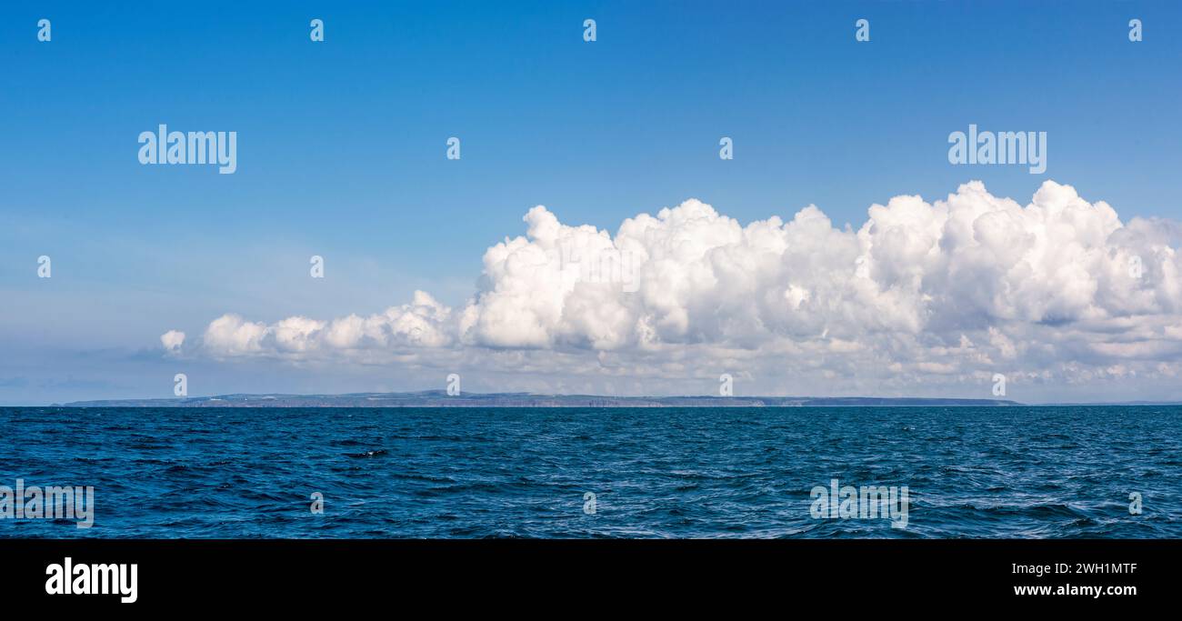 Erster Anblick von Land's End, Cornwall, Großbritannien von einer Yacht aus, mit einer Kumuluswolke über dem Land: Panoramaaufnahme. Stockfoto