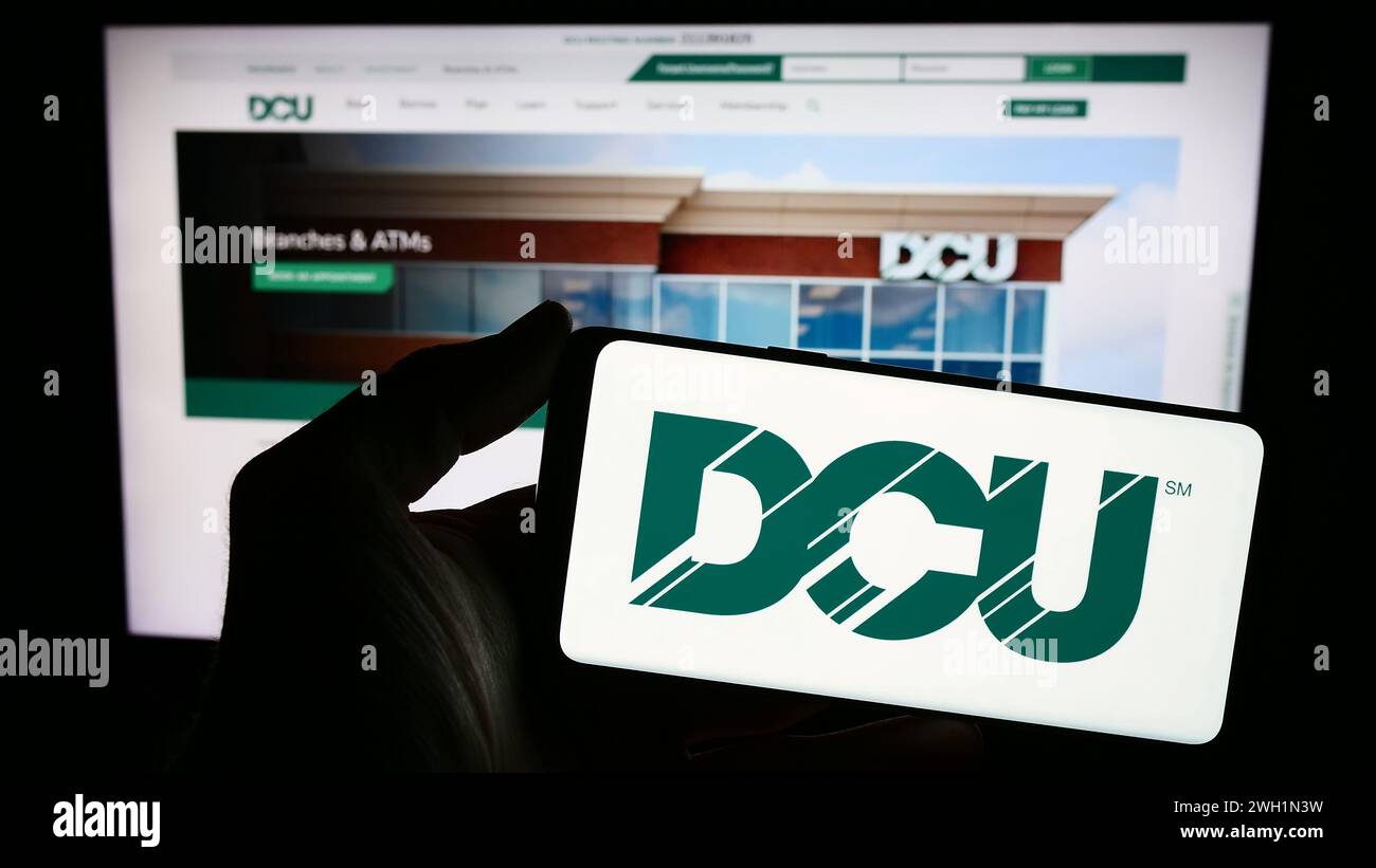 Person mit Smartphone und Logo des Finanzinstituts Digital Federal Credit Union (DCU) vor der Website. Schwerpunkt auf dem Display des Telefons. Stockfoto