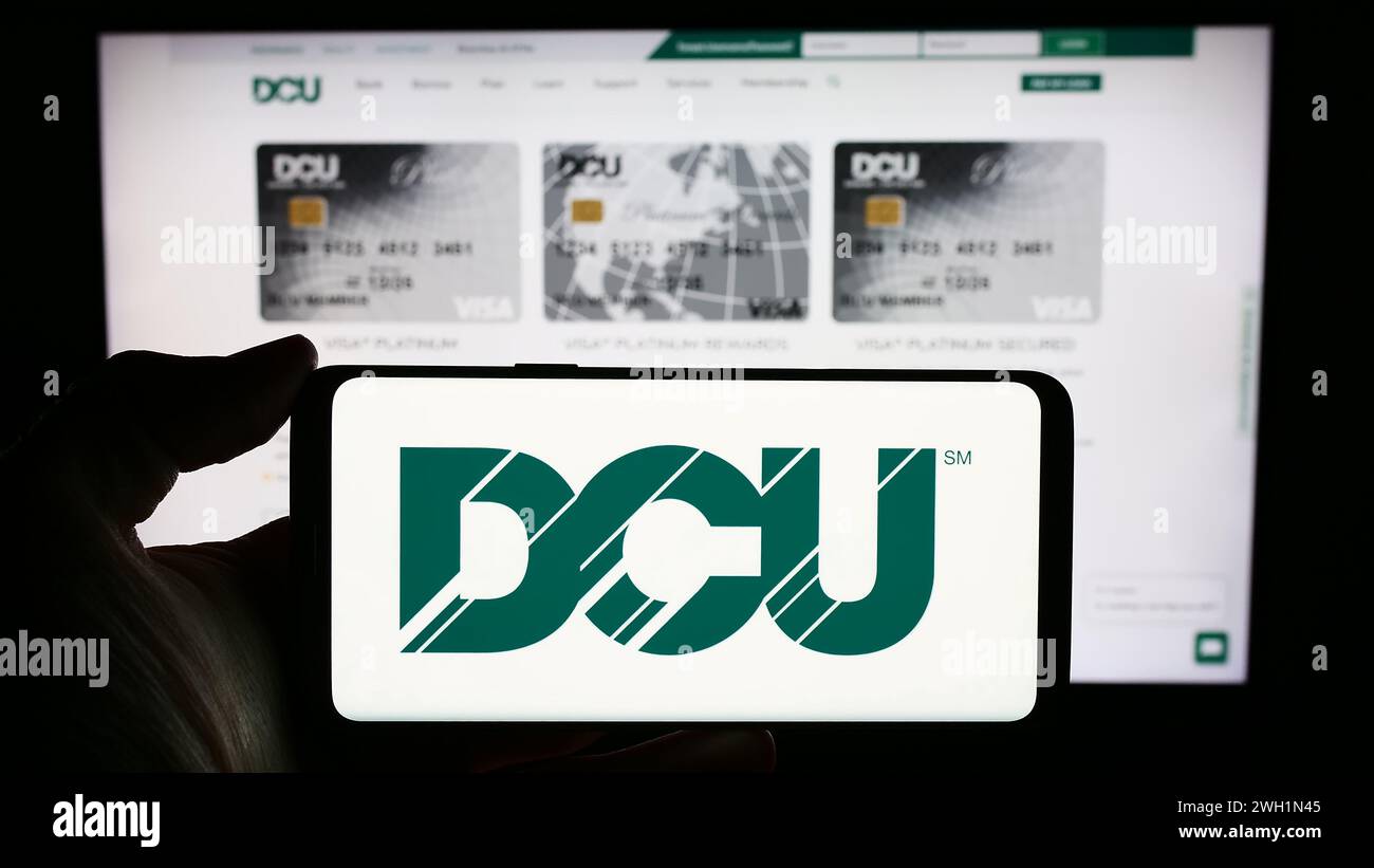 Person mit Mobiltelefon mit Logo des Finanzinstituts Digital Federal Credit Union (DCU) vor der Webseite. Schwerpunkt auf dem Display des Telefons. Stockfoto