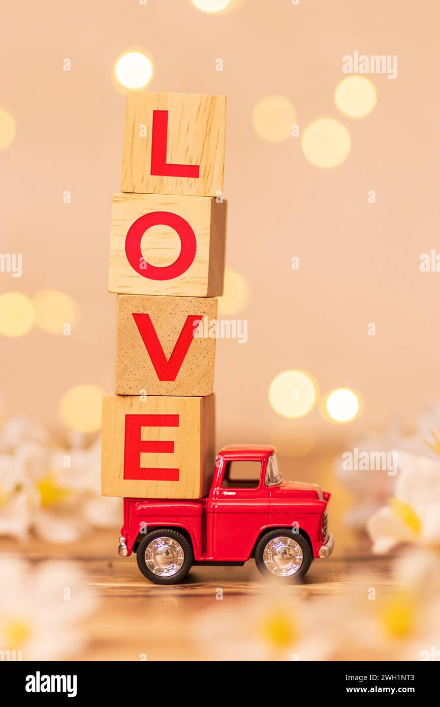 Rotes Truck-Spielzeug mit Holzwürfel und Text Love auf der Rückseite des Pickups, um Liebe zum Valentinstag mit weißem Blumenfeld zu liefern Stockfoto