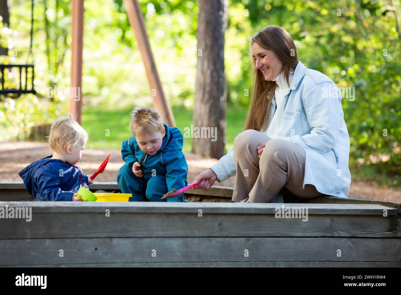 Die Mutter mit zwei Kindern macht Spaß auf dem Spielplatz. Zwei kleine Jungs mit ihrer Mutter, die in der Sandbox spielt Stockfoto