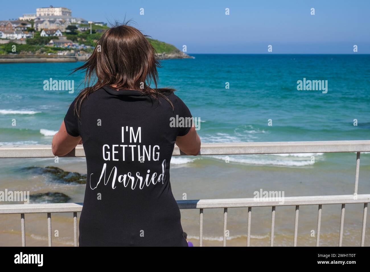 Eine Frau, die ein T-Shirt mit I'm Get Married trägt, bedruckt auf der Rückseite, um Towan Beach in Newquay in Cornwall in Großbritannien zu sehen. Stockfoto