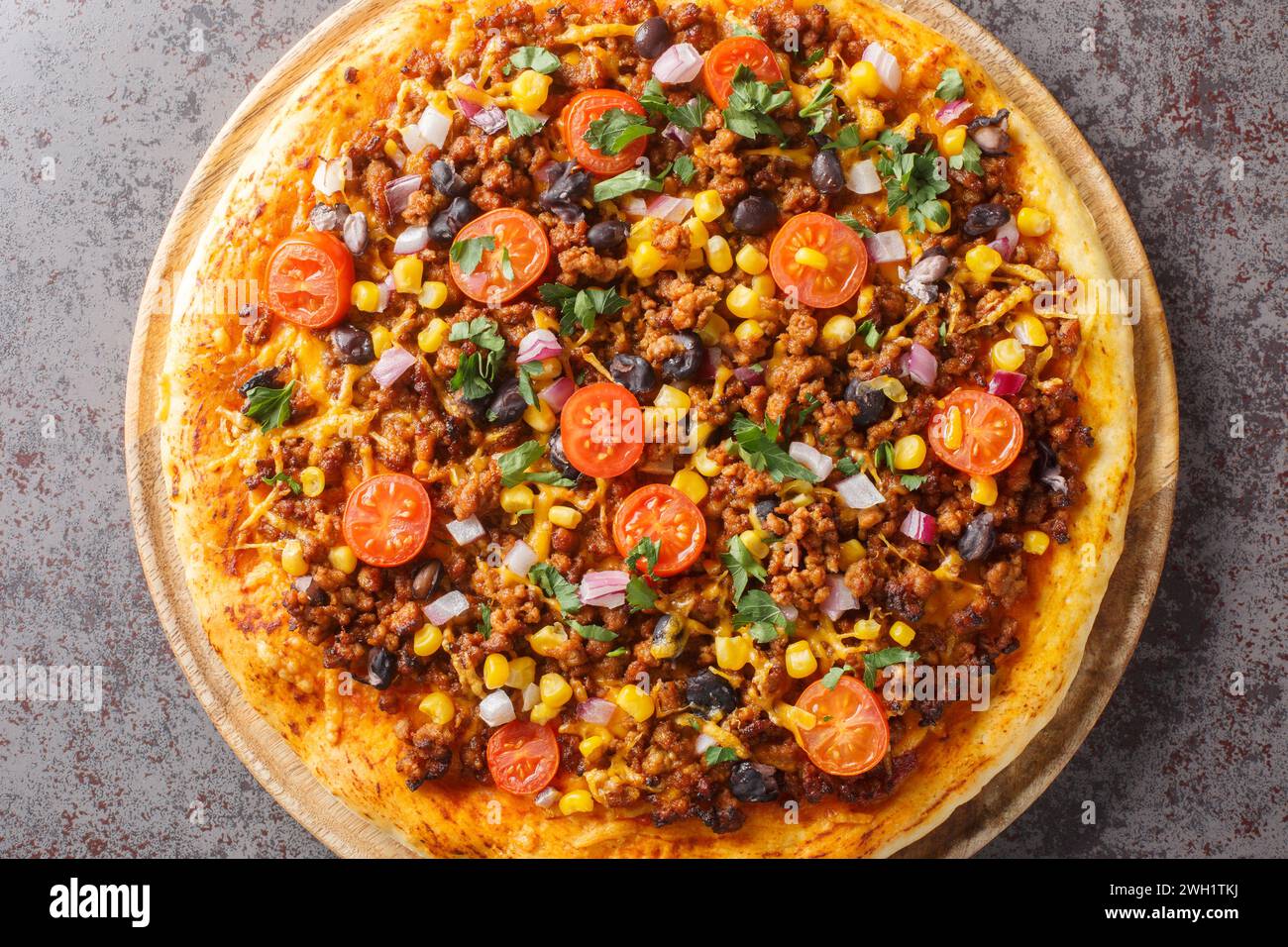 Hausgemachte Tex-Mex-Pizza mit Hackfleisch, Gemüse, Cheddar-Käse und mexikanischen Gewürzen auf einem Holzbrett auf dem Tisch. Horizontale Draufsicht fr Stockfoto
