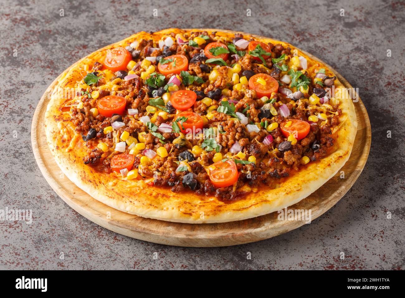 Hausgemachte Tex-Mex-Pizza mit Hackfleisch, Gemüse, Cheddar-Käse und mexikanischen Gewürzen auf einem Holzbrett auf dem Tisch. Horizontal Stockfoto