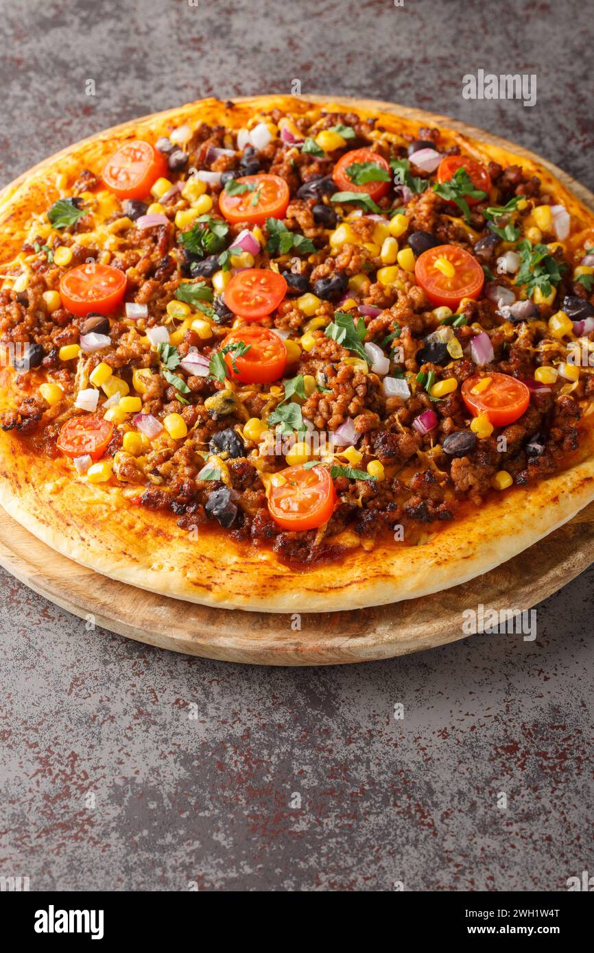 Hausgemachte, scharfe mexikanische Taco-Pizza mit Hackfleisch, Tomaten, Mais, schwarzen Bohnen, Cheddar-Käse, rote Zwiebel auf dem Holzbrett auf dem Tisch. Vertikal Stockfoto