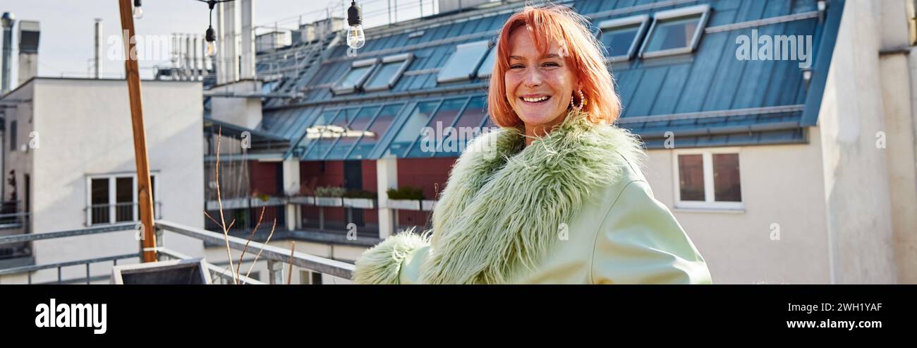 Zufriedene Frau in stilvoller Freizeitkleidung, die auf der Dachterrasse in Wien in die Kamera schaut, Banner Stockfoto