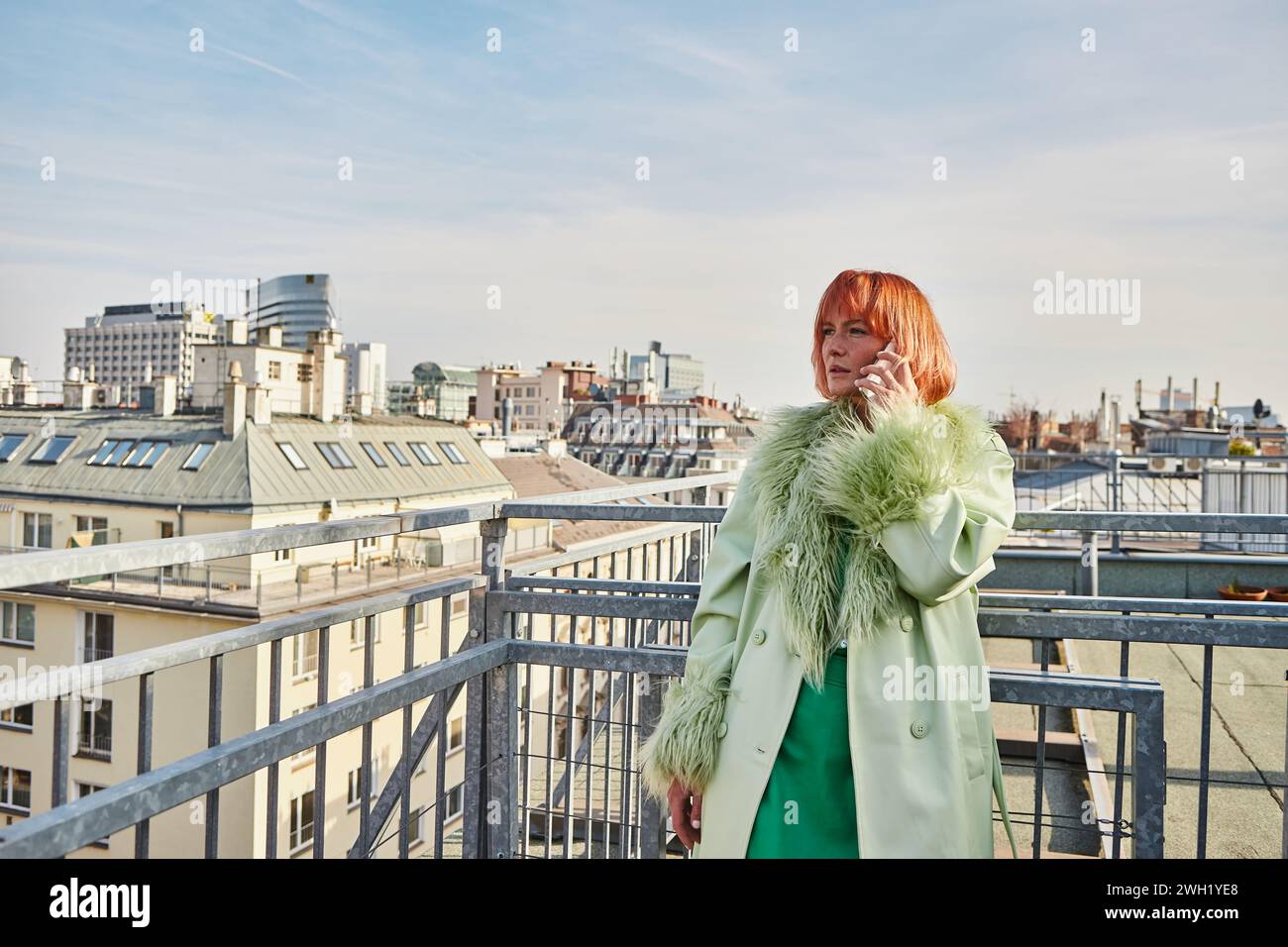 Verführerische Frau in stilvoller Freizeitkleidung, die auf dem Handy auf der Dachterrasse in Wien spricht Stockfoto