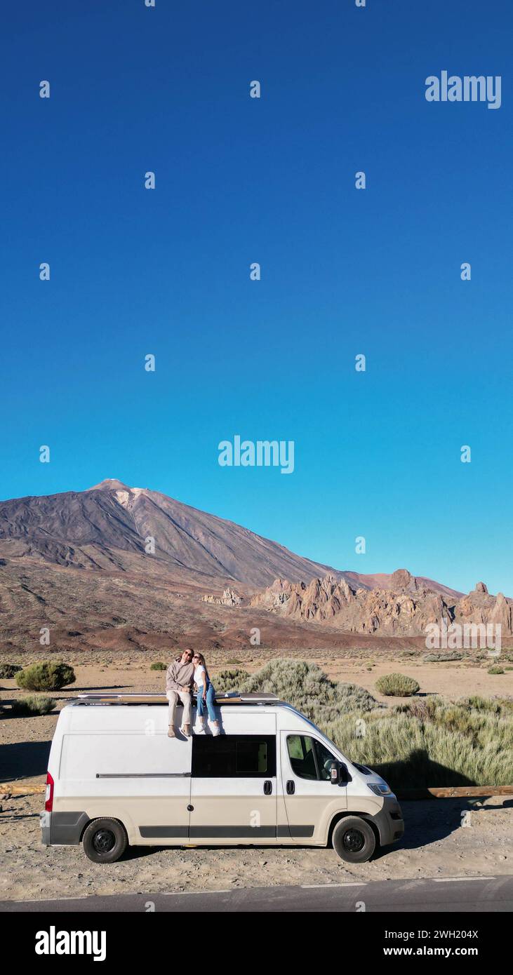 Zwei Personen sitzen auf einem Minibus, der auf dem Teide-Vulkan auf Teneriffa geparkt ist und die malerische Aussicht genießen. Stockfoto