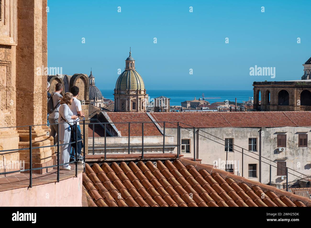 Eine Gruppe von Menschen, die in Sommerkleidung gekleidet sind, steht auf einem Balkon mit Blick auf die belebte Stadt palermo, deren Blick auf die majestätische Kathedrale A gerichtet ist Stockfoto