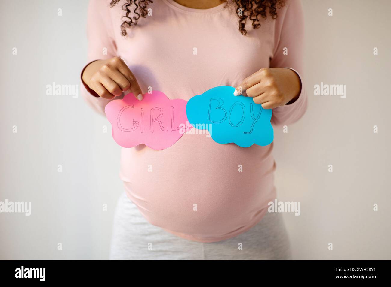 Schwangere Frau mit rosa und blauen Papierwolken mit „MÄDCHEN“ und „JUNGEN“ Stockfoto