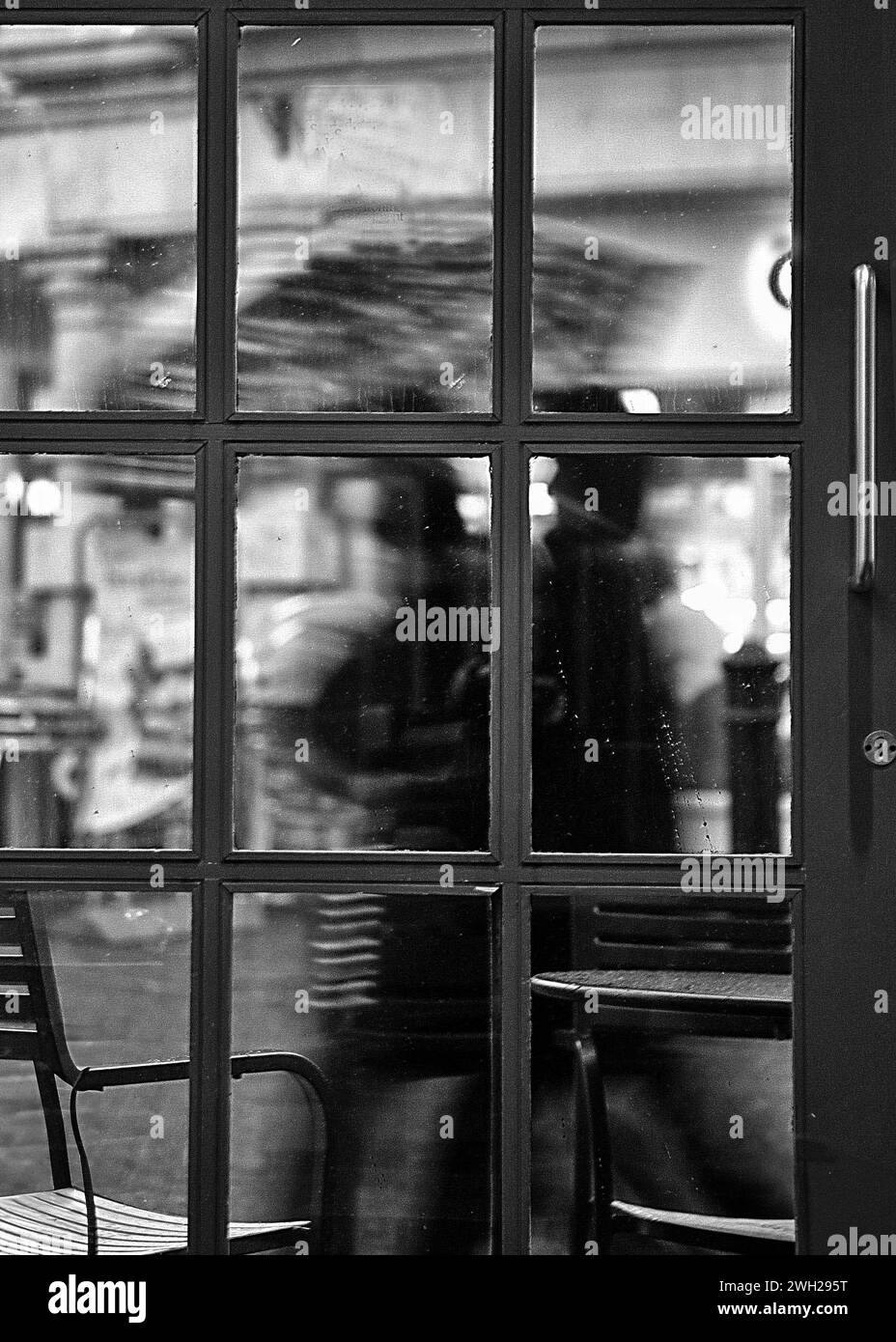 Ein abstraktes Schwarzweiß-Bild, das durch eine Cafetür auf Leute blickt, die im Regen mit Sonnenschirmen vorbeilaufen Stockfoto