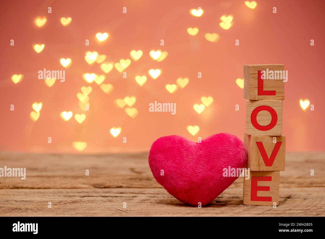 Holzwürfel mit rotem Text Love und kleinem rosa flauschigem Herz Platz neben auf Holztisch mit Kopierraum, defokussiertes herzförmiges Bokeh-Licht Stockfoto