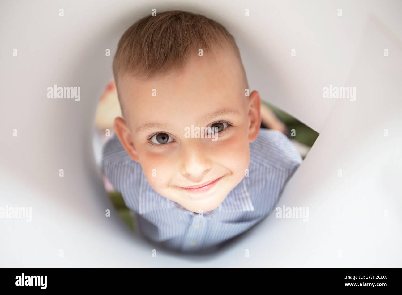 Das Gesicht eines lustigen kleinen Jungen, der in ein Papierloch schaut. Stockfoto