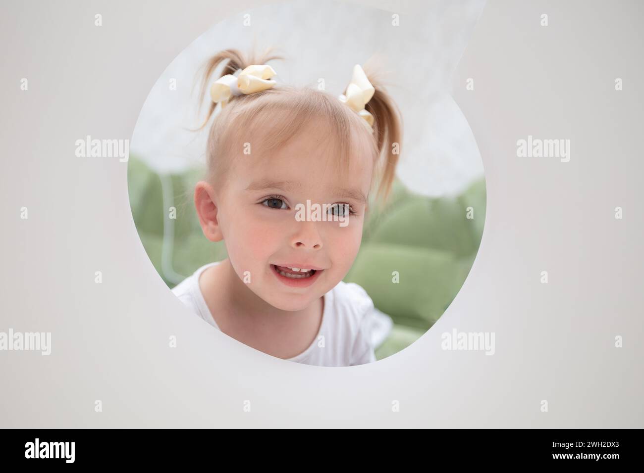 Das Gesicht eines lustigen kleinen Mädchens, das in ein Loch aus Papier schaut. Stockfoto