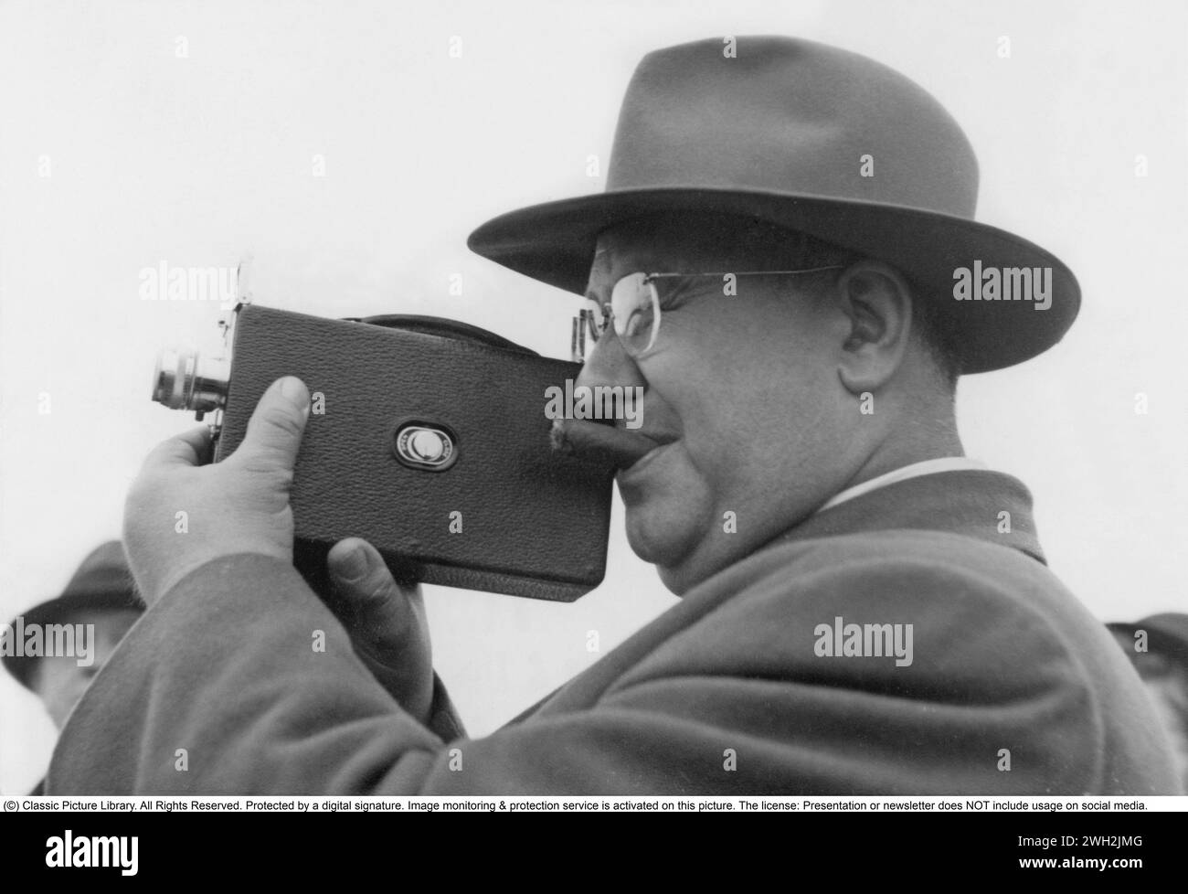 In den 1940er Jahren Ein Mann filmt mit einer Amateurkamera. Der Film wurde dann entwickelt und auf einem Filmprojektor auf einer zusammenklappbaren Leinwand zu Hause gezeigt. Der Film hatte keinen Ton. Die Filmkameras waren nicht batteriebetrieben und man musste sie wie eine Uhr aufwickeln, damit sie funktionieren. Stockholm Schweden 1946 Stockfoto