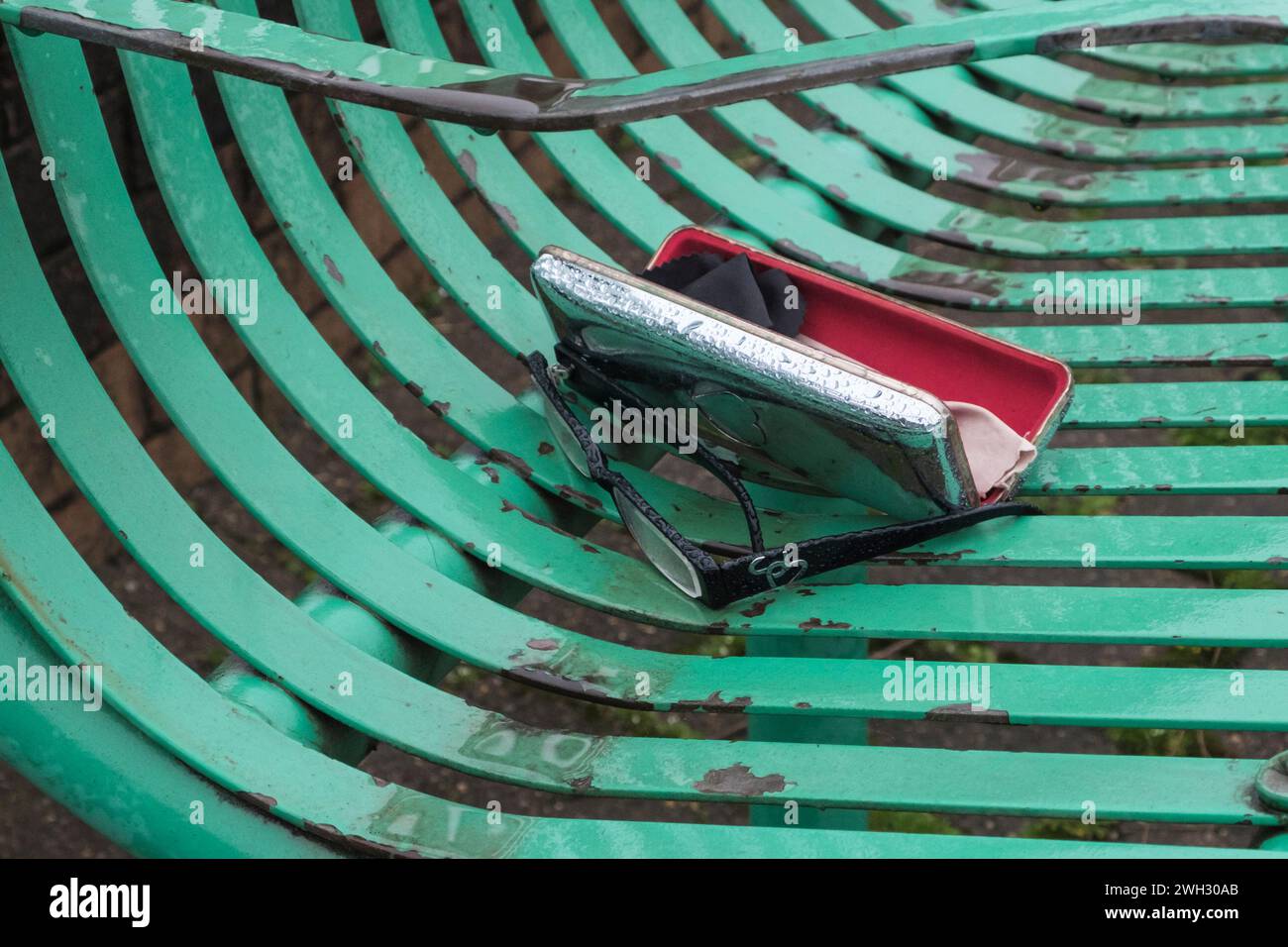 Brille oder Brille und Tasche, verloren auf einer Parkbank aus Metall Stockfoto