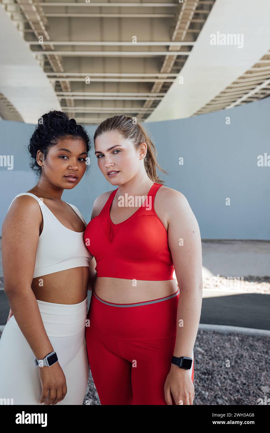 Porträt zweier weiblicher Athleten in Übergröße, die draußen stehen und in die Kamera schauen. Zwei junge Frauen in Fitnesskleidung stehen zusammen. Stockfoto