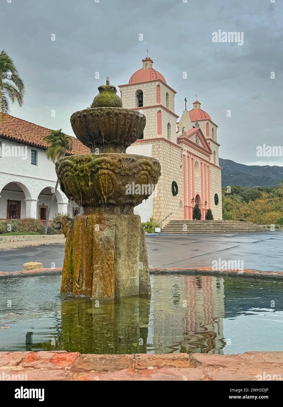 Santa Barbara, CA, USA - 18. Dezember 2023: Nahaufnahme des maurischen Brunnens an der Seite des Old Mission Church Building unter graublauem Himmel. Reflexion im Wasser Stockfoto