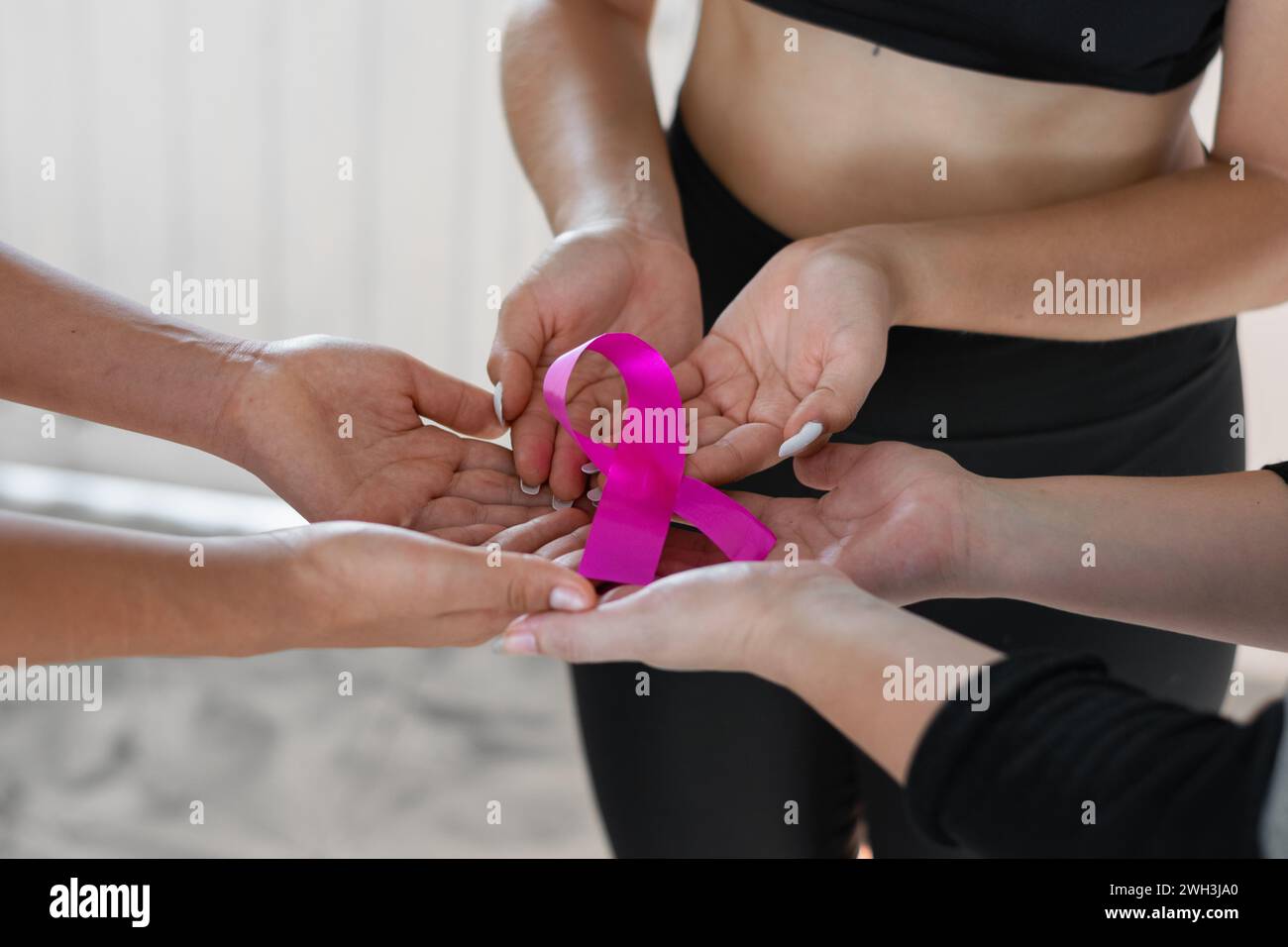 Eine Gruppe von Frauen, die sich an den Händen zusammenschließen, um ein rosafarbenes Band zu halten, Symbol für den Kampf gegen Brustkrebs. Stockfoto