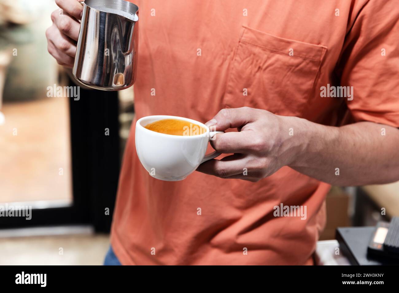 Hände des Barista, die Cappuccino in einer kleinen weißen Tasse zubereiten Stockfoto