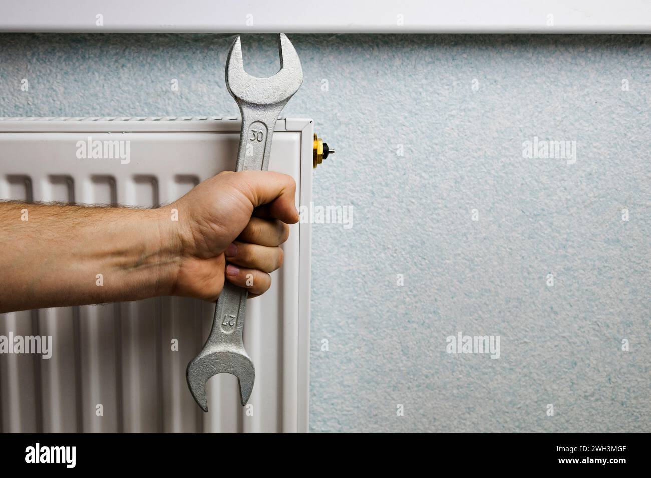 Ein Mann montiert einen Heizkörper an der Wand. Das Konzept der Hausrenovierung. Heizungsabschaltung, Wärmeprobleme Stockfoto Ein Mann montiert einen Heizkörper an der Wand. Das Konzept der Hausrenovierung. Heizungsabschaltung, Wärmeprobleme Stockfoto
