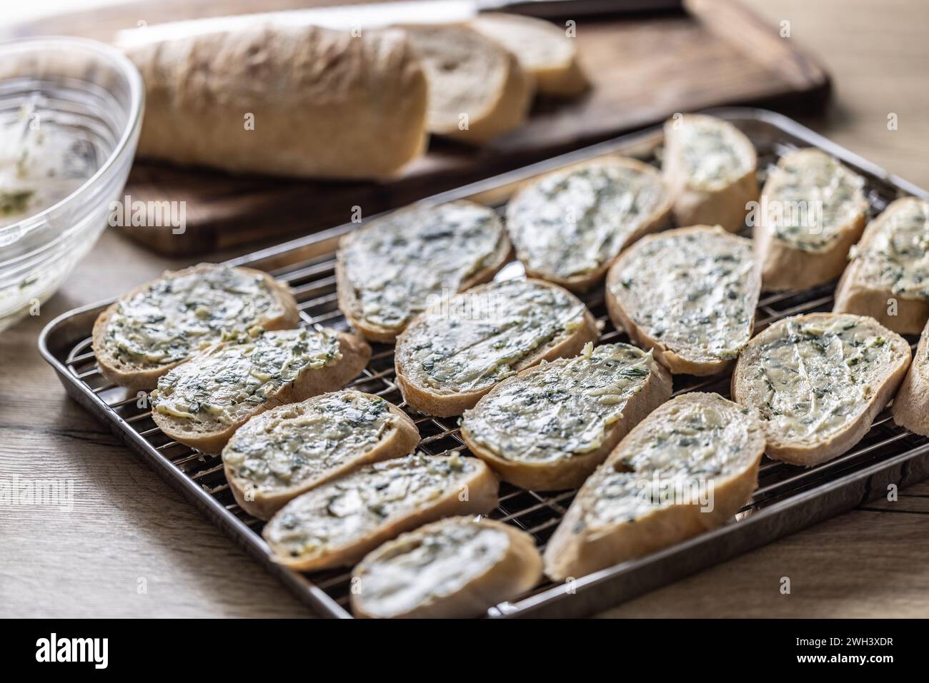 Mini-Baguettes mit Kräuter-Knoblauchbutter, fertig zum Backen auf einem Tablett. Stockfoto