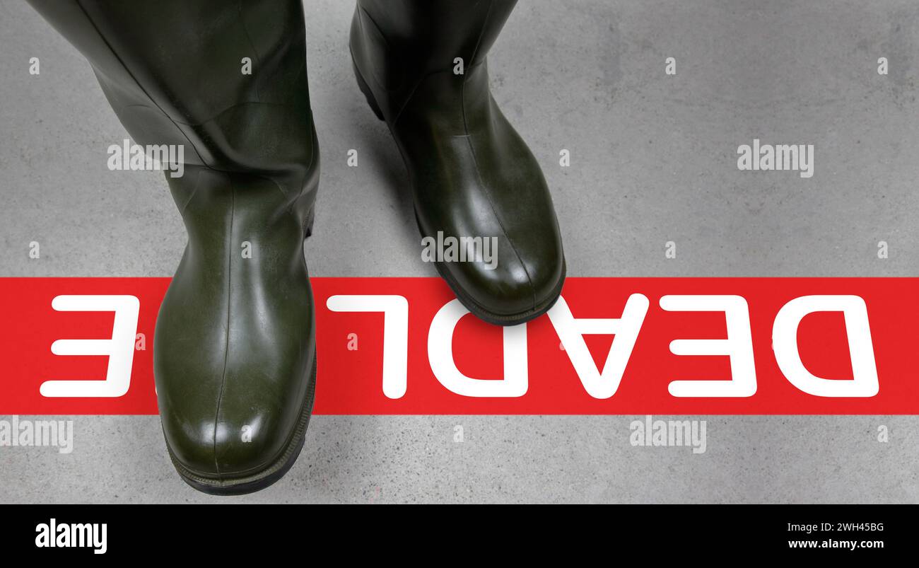 Eine rote Linie markiert die Frist. Militärische Gummistiefel kreuzen sie entschieden. Die Zeit tickt, Entscheidungen werden kritisch. Stockfoto